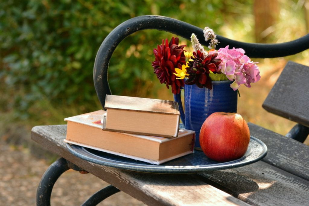 Books, flowers, and apple on a bench